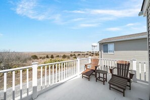 A covered outdoor area with a white railing, two wooden Adirondack chairs, and a small table.