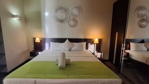 A hotel room with a large bed, two bedside lamps, a green bedspread, and decorative wall art.