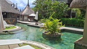 A resort pool with thatched-roof structures, lounge chairs, and tropical plants.