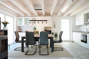 A modern kitchen with a dining area, featuring a central island, pendant lighting, and a large window.