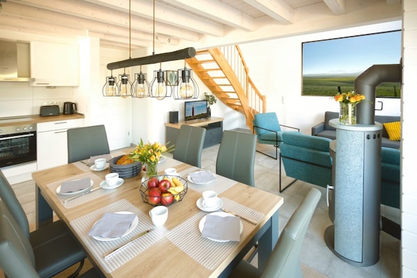 A modern kitchen with a built-in oven, a dining area with a wooden table set for four, and a large window overlooking a scenic landscape.