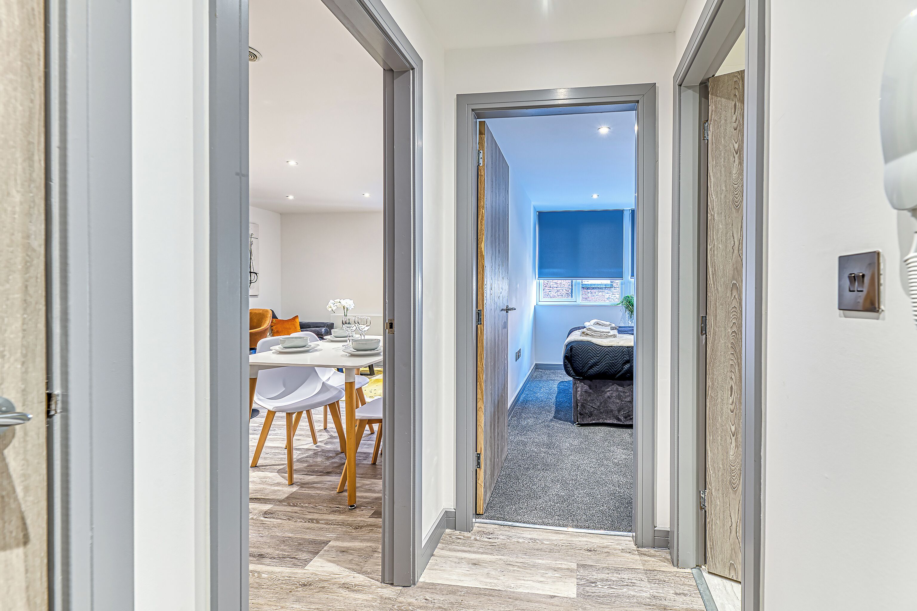 A hallway leading to a dining area with a table and chairs, a sofa, and a view of the outside.