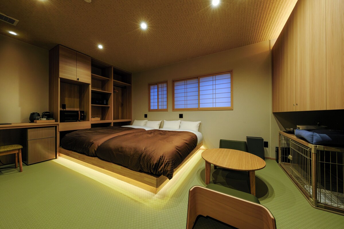 Quarto com cama, mesas de cabeceira, escrivaninha, cadeira e uma pequena mesa.