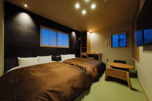 Een hotelkamer met een groot bed, een bureau en een stoel. Er zijn twee ramen en een televisie aan de muur.