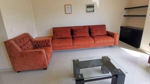 Ein Wohnzimmer mit einer Couch, einem Glastisch, einem Deckenventilator und einer schwarzen Unterhaltungsecke.