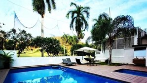 Ein Swimmingpool mit Liegestühlen und einem Tisch, umgeben von Palmen und einem weißen Gebäude.