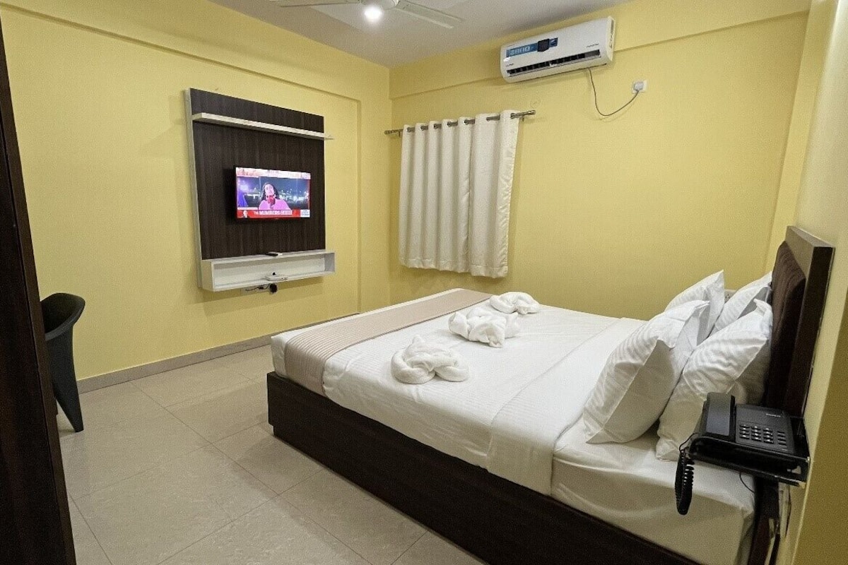 A hotel room with a bed, a TV mounted on the wall, a telephone, and a curtain.