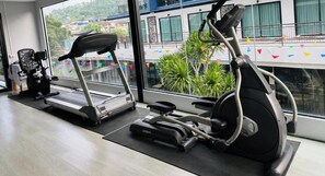 Een sportschool met loopbanden en een hometrainer, grote ramen met uitzicht op gebouwen en groen.