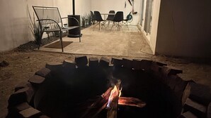 Eine Terrasse im Freien mit Feuerstelle, Lichterketten und einem Tisch mit Stühlen.