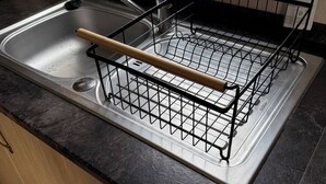Una cocina con un lavamanos de acero inoxidable, un escurreplatos, una tetera y una botella de detergente.