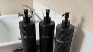 Tres botellas negras con dosificadores sobre una encimera oscura en un baño.
