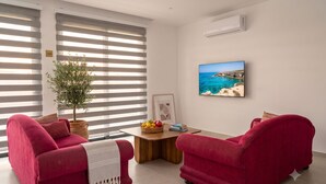 Ein Wohnzimmer mit zwei roten Sofas, einem Holztisch mit Obst, einer Topfpflanze und einem gerahmten Bild an der Wand.