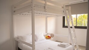 Ein Stockbett mit einer Leiter, ein Nachttisch mit Obstschale und ein Fenster mit Blick auf Grünflächen.