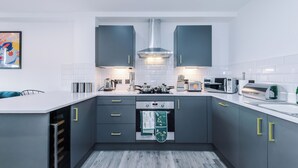 Una cocina moderna con armarios grises, encimeras blancas, horno integrado y campana extractora de acero inoxidable.