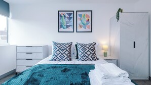 Un dormitorio moderno con cama, dos almohadas, una mesita de noche, lámpara, armario y dos obras de arte abstracto en la pared.