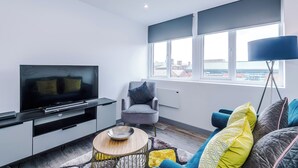 Una sala de estar moderna con un televisor de pantalla plana, un sillón gris, un sofá azul y un ventanal grande.