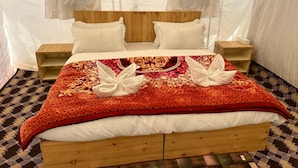 Een bed met een houten hoofdeinde, twee nachtkastjes, een geborduurde deken en twee handdoeken gevouwen in de vorm van zwanen.