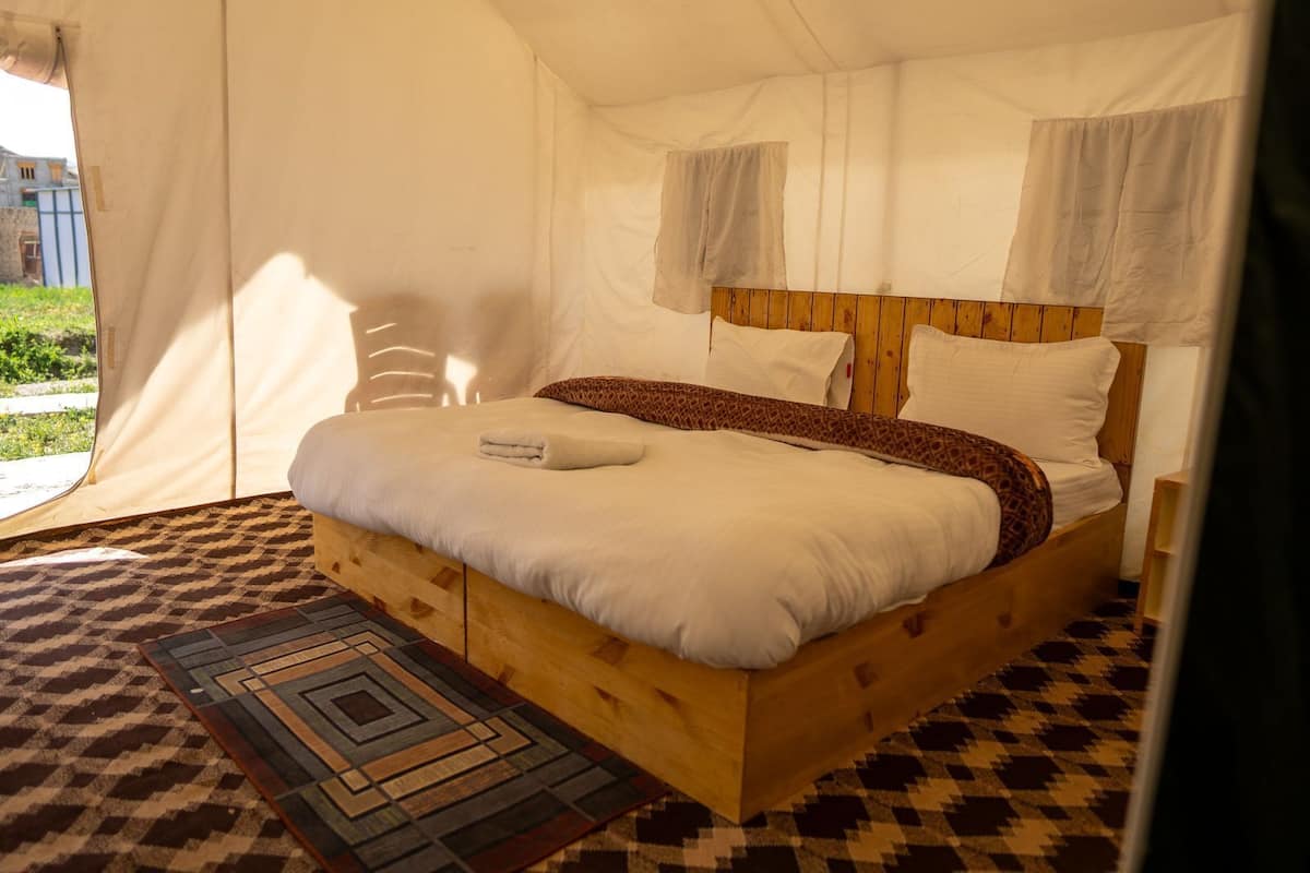 Un dormitorio tipo tienda de campaña con una cama de madera, ropa de cama blanca y un tapete estampado.