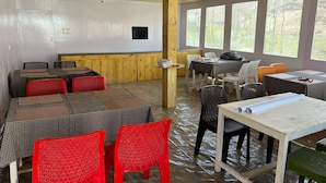 Een eetgedeelte met tafels, stoelen, een houten plafond en grote ramen.