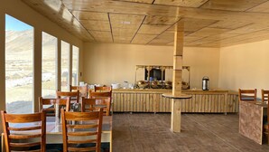 Een houten interieur met tafels en stoelen, een centrale kolom en uitzicht door grote ramen.