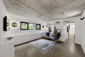 A modern interior with a concrete ceiling, a large window with a view of greenery, a patterned rug, and a seating area with a chair and a sofa.