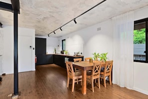 A modern kitchen with wooden cabinets, a dining table with chairs, and a view of greenery outside.