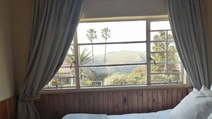 Un dormitorio con una cama grande, paneles de madera, una ventana con cortinas y vistas a la vegetación.