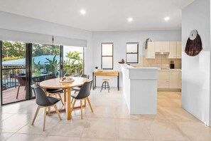 A modern kitchen with white cabinets, a central island, and a dining area with a round table and chairs. - Avenal Noosa Views, Pool, Walk to Hastings St (Noosa Region)