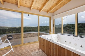A modern bathroom with a large bathtub, wooden flooring, and large windows offering a scenic view. - Cretan Traditional Home Villa with Mountain View, Wi-Fi, and Air Conditioning (Tilisos)