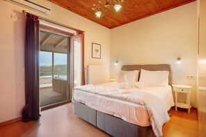 Une chambre à coucher avec un lit, des tables de chevet, un ventilateur de plafond et une vue sur l’extérieur, visible à travers une porte vitrée.