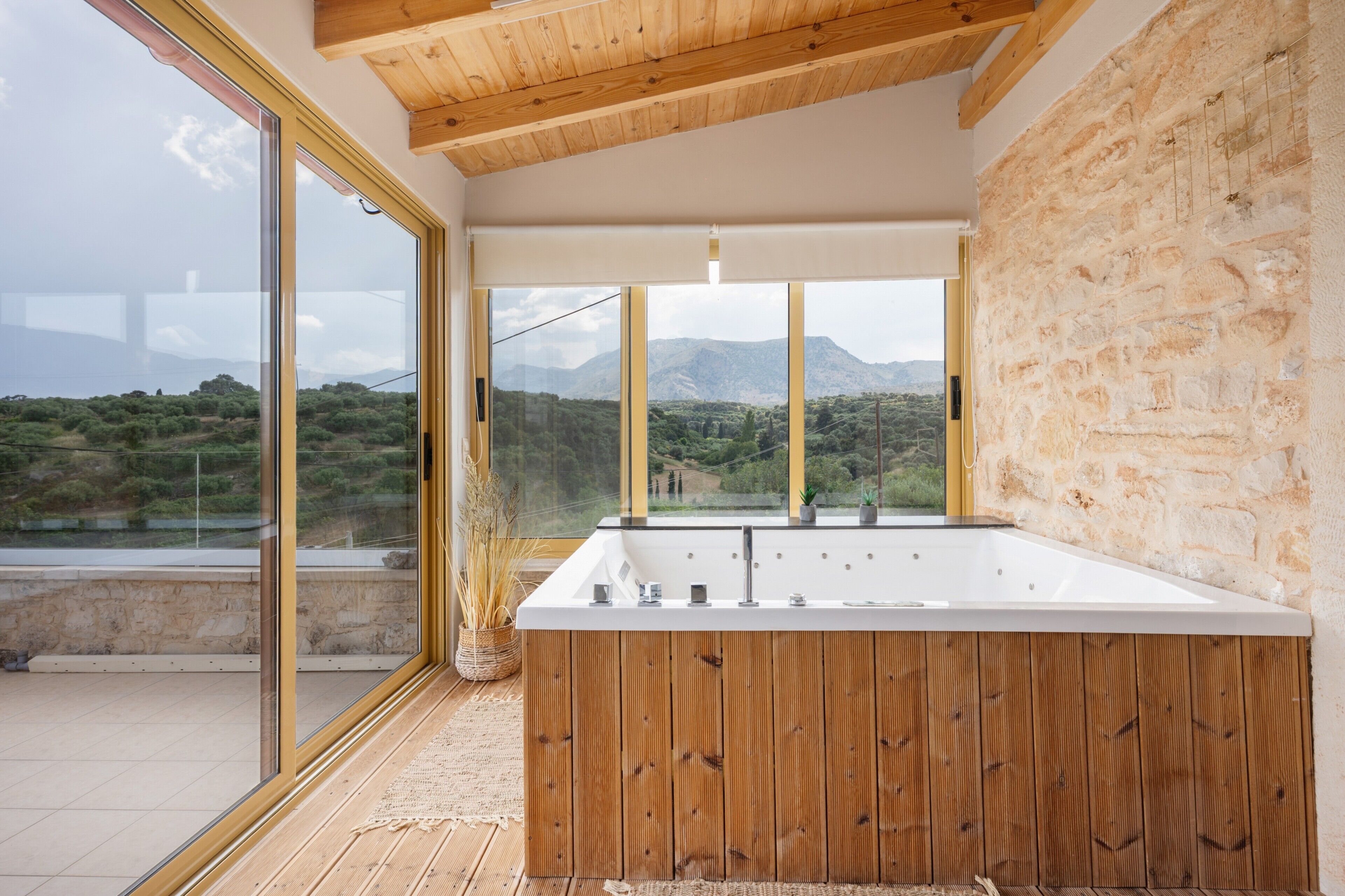 A modern bathroom with a large bathtub, wooden accents, and a view of a mountainous landscape through large windows.