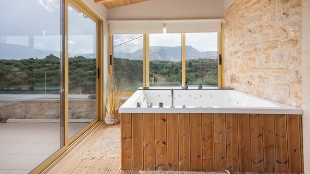 Ein modernes Badezimmer mit einer großzügigen Badewanne, Holzdetails und Blick auf eine Berglandschaft durch große Fenster.