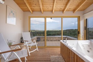 A modern room with a wooden ceiling, a large sliding glass door, a hot tub, and two white chairs. - Cretan Traditional Home Villa with Mountain View, Wi-Fi, and Air Conditioning (Tilisos)
