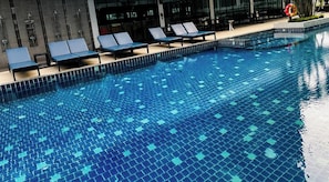 Une piscine dont le fond est carrelé et qui est bordée de chaises longues.