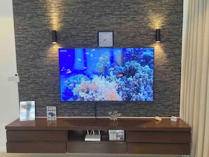 Ein Fernseher an einer Steinwand befestigt, darüber eine Uhr und darunter ein Unterhaltungsschrank aus Holz.