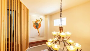 Una escalera con barandilla de madera, un cuadro colgado en la pared de un artista marcial y una araña con múltiples luces.