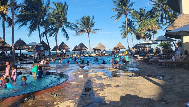 A pool area with palm trees, umbrellas, and lounge chairs.