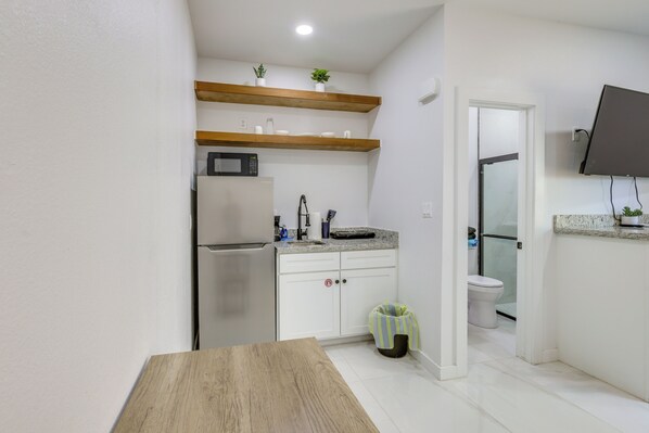 A compact kitchen with a refrigerator, microwave, and wooden shelves. - Reel & Relax! Pet-Friendly SPI Stay Next to Beach (South Padre Island)