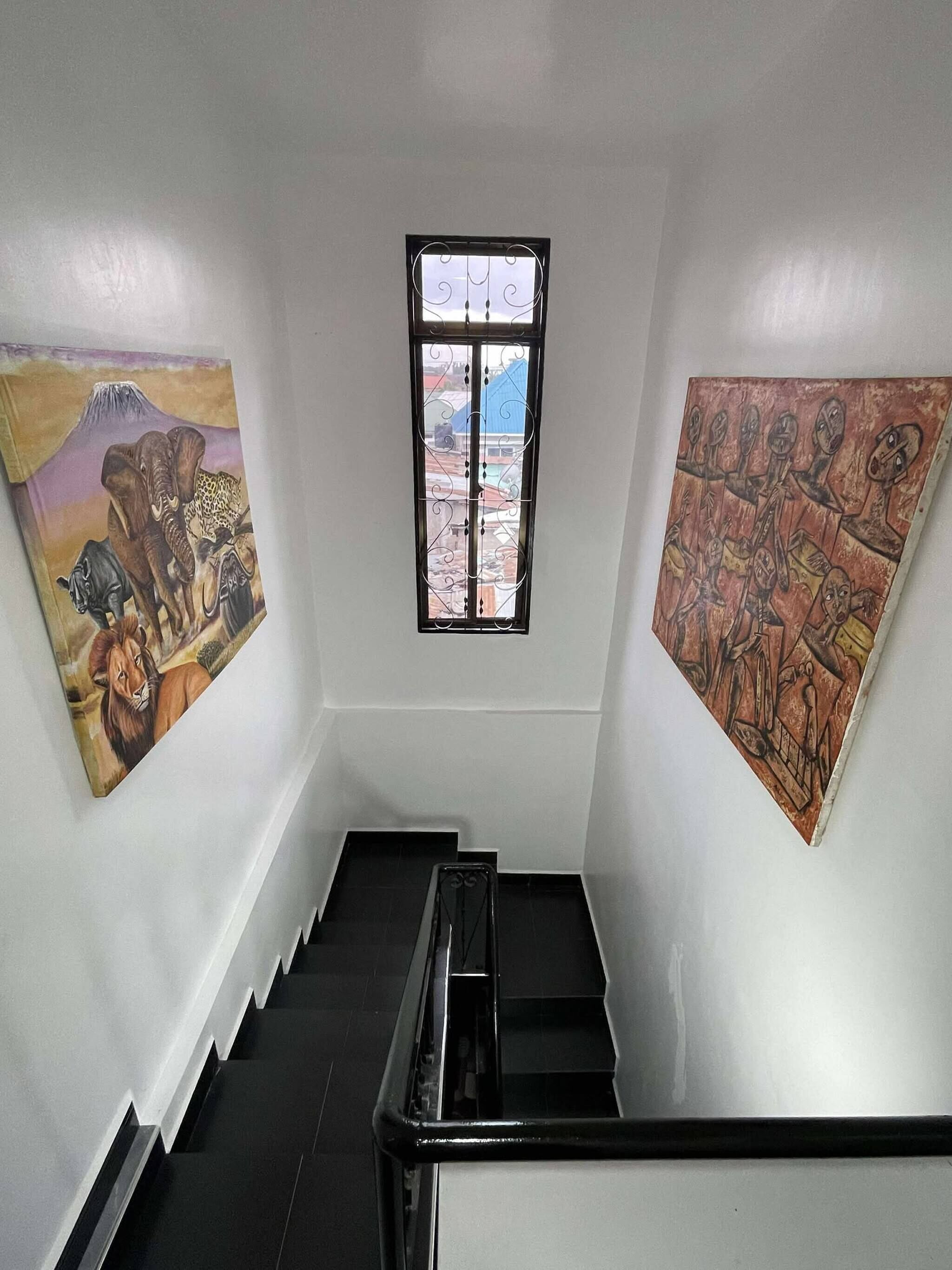 A staircase with a metal handrail, a window with decorative bars, and two paintings on the walls.