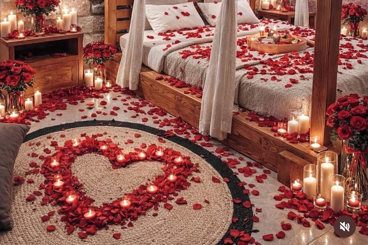 A romantic bedroom with a stone wall, a canopy bed, rose petals, candles, and a heart-shaped rug.