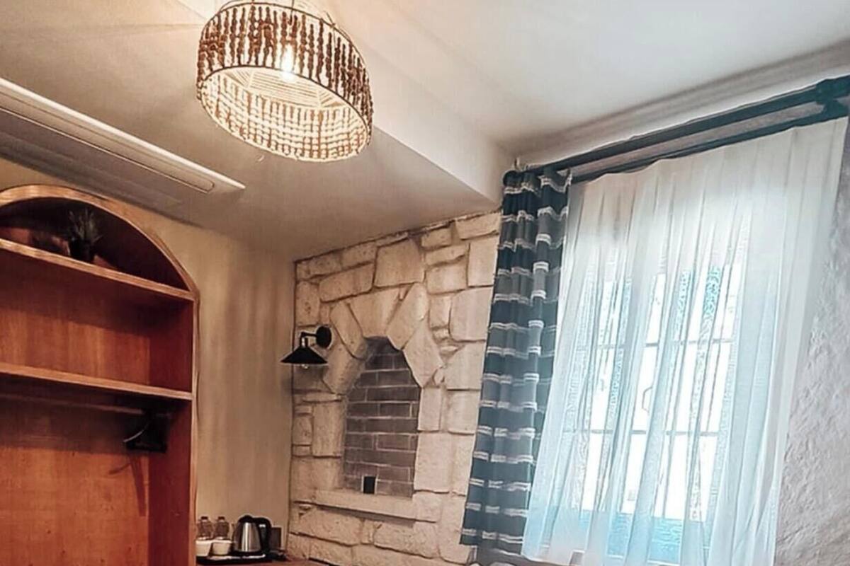 A bedroom with a stone wall, a wooden wardrobe, a bed with patterned bedding, and a hanging light fixture.