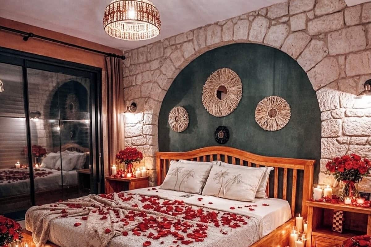 A bedroom with a stone wall, a wooden bed, and a chandelier.