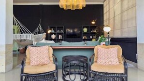 Un espace de vie comprenant des fauteuils en osier, un fauteuil suspendu, un téléviseur et une bibliothèque.