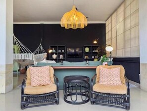A living area with wicker chairs, a hanging chair, a TV, and a bookshelf. - Rumah Rama 3BR Private Pool Villa• Surrounded by Best Beaches in Bali (Kuta utara)