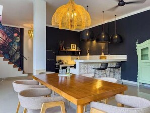 A modern kitchen with a dining area, featuring a wooden table, chairs, pendant lights, and a staircase with a floral mural. - Rumah Rama 3BR Private Pool Villa• Surrounded by Best Beaches in Bali (Kuta utara)