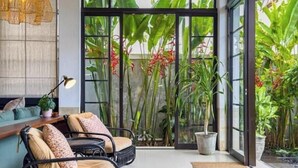 Un intérieur moderne avec des meubles en osier, une porte vitrée donnant sur un jardin et un luminaire en fibres tressées.