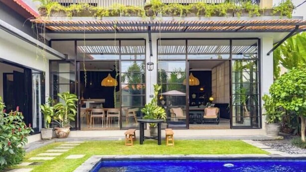 Une maison moderne dotée d’une piscine, de portes vitrées et d’un espace salon extérieur.