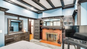 Quarto com cama, penteadeira, televisão, lareira e um espelho grande.