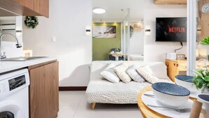 Una sala de estar moderna con un sofá, televisor, zona de cocina con lavadora y mesa de comedor con cuencos.