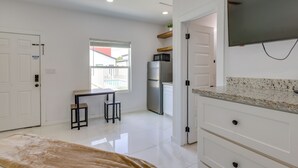 Una cocina moderna con armarios blancos, encimera de granito, refrigerador de acero inoxidable y televisor de pantalla plana montado sobre la encimera.